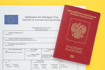 Schengen visa application form in English and Russian language and passport on yellow background....