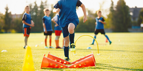 School kids jumping over obstacles on the training pitch. Group of children in sports soccer training. Boys improving agility skills on sport class