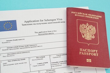 Schengen visa application form in English and Russian language and passport on blue background. Prohibition and suspension of visas for tourists to travel to European Union and Baltic States concept