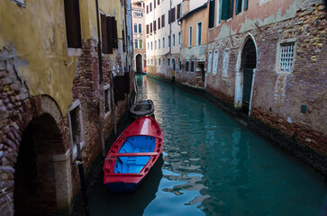 Fototapeta na wymiar Una piccola imbarcazione rossa e blu ormeggiata in uno stretto canale di Venezia