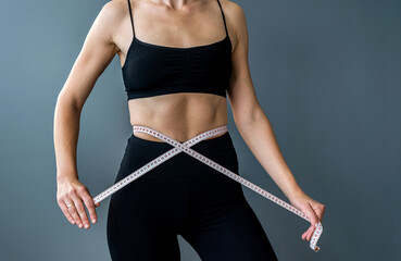fit woman measuring with tape measure  measuring waist after dieting isolated over gray