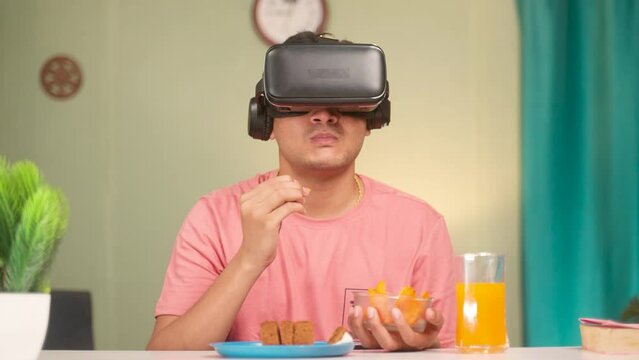 young man with vitual reality headset or goggles eating food while watching videos or experiencing Metaverse or virtual world at home - concept of futuristic, modern lifestyle and technology addiction