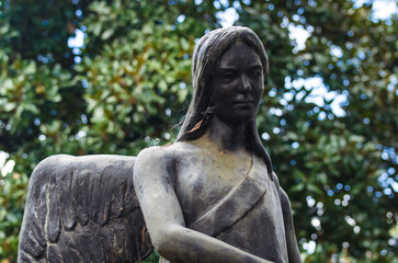 La statua bronzea di un angelo su una tomba dell cimitero maggiore di Milano con degli alberi sullo...