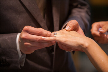 Close up of loving bride and groom putting a beautiful wedding ring to the beloved partner, marry me concept. High quality photo