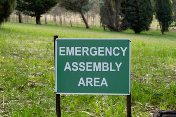 Road sign Emergency Assembly Area plate white on green in the park in Australia