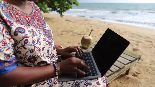 Close up of a woman using a laptop at a tropical beach, black screen for copy space.