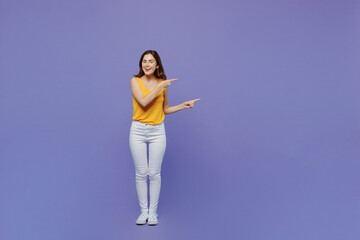 Full body young fun woman 20s she wear yellow tank shirt point index finger aside on workspace area mock up isolated on plain pastel light purple background studio portrait. People lifestyle concept.