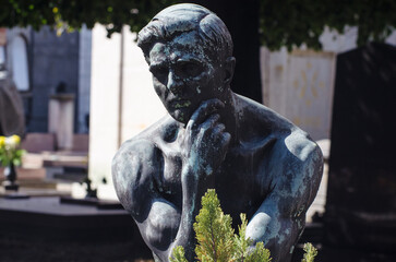 La statua bronzea di un uomo che pensa su una tomba del cimitero maggiore di Milano