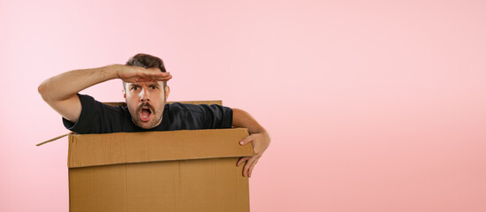 Funny emotive man sitting inside carton box and looking for big sales isolated on pink background....