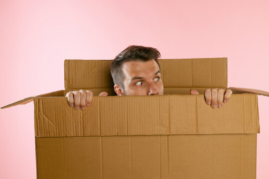 Portrait of funny man peeking out carton box isolated on pink background