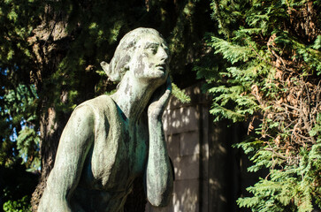 Primo piano di una statua in bronzo di una donna dolente con un fiore in mano su una tomba del cimitero maggiore di Milano