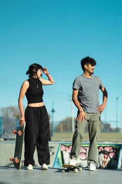 Girl and boy skate boarders standing with their skates on beautiful sunny day.