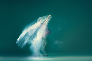 Ghostly vision. Tender girl, ballet dancer dancing with white cloth isolated on green background....