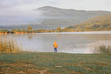 The boy is standing by the autumn lake.
