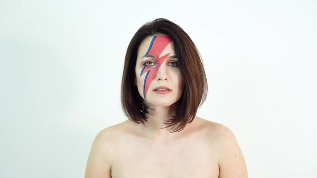 red and blue lightning bolt on her beautiful face. Beautiful girl with original make-up on a white background. Studio photo.