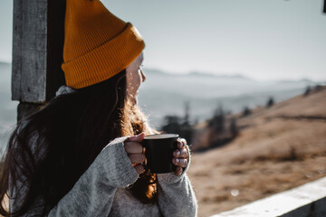 Woman with cup of coffee is sitting in front of mountain view and look away