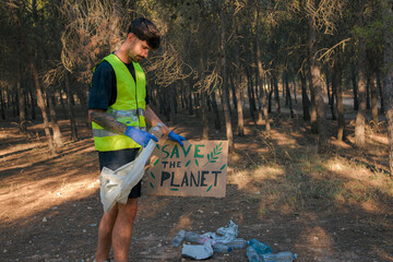 Man in reflective vest holding a sign and picking up plastic trash in a forest