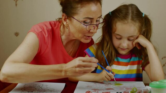 Grandmother teaches her granddaughter how to paint. Preschool education.