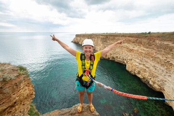 Young woman jump from the cliff with a rope. Ropejumping.