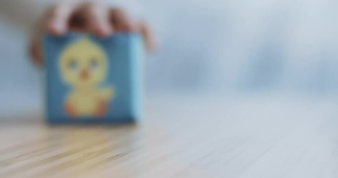 Close-up of a children's plush cube with the image of a chicken. The cube is on the left. A man moves the cube back and forth. 