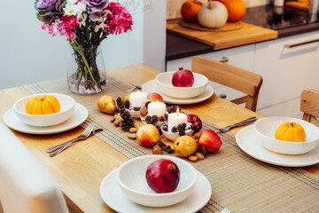 Fall table setting for celebration Thanksgiving day family party. Autumn composition with candles, fruits, nuts and cones. Plates with pumpkins and pomegranate. Natural autumn decor. Selective focus