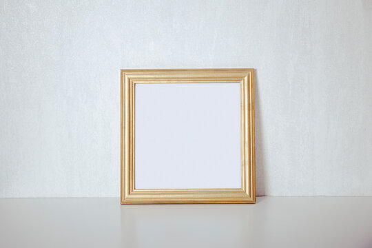  Empty gold frame on a white background near the wall, minimalistic blank for an inscription
