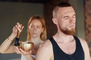 Woman helps man to tune in to a nail-standing session and conducts a meditation session with the help of a Tibetan bowl