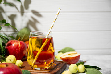 Glass of apple juice and apples in the garden under sunlight. The concept of harvesting the autumn harvest of apples, copy space for text