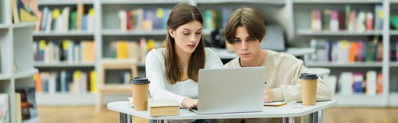 teenage friends looking at laptop while studying in library reading room, banner.