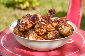 Meat on barbecue grill. Grilled chicken legs in a bowl. Cooked fried chicken drumsticks on a blurred background in the garden. Shallow depth of field