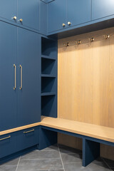 A mudroom with blue cabinets and wood cabinets and a grey tiled floor.