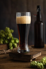 Beer. A tall glass glass of beer, with foam, with hops on an old wooden board. Beer concept. Oktoborfest. Vintage.
