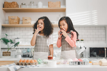 Children enjoy cooking in the kitchen. Happy Asian kids decorating the cake, bake cookies in the kitchen. Two cute little diversity girls play and learn trough the experience. Education concept.