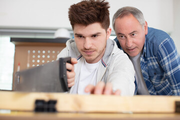 apprentice carpenter using a saw under supervision