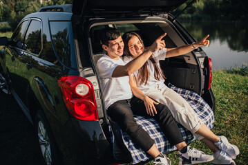 Young happy couple sitting in car trunk outdoor