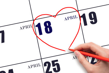 A woman's hand drawing a red heart shape on the calendar date of 18 April. Heart as a symbol of love.