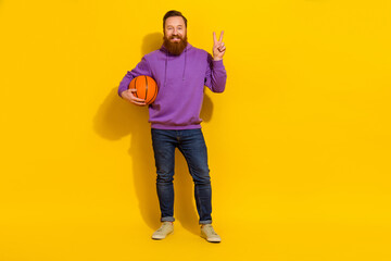 Full length photo of funky cute man wear violet sweatshirt showing v-sign holding ball isolated...