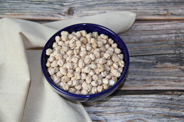 Chickpeas (Cicer arietinum) in a blue bowl, on a wooden table, top view. It is also known by the names: Gravanço, Herbanzo, Chicken Pea or Bengal Pea or Duck Grain.