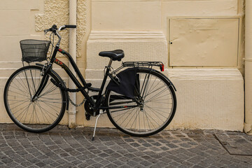 A black woman’s bicycle with basket parked against a wall in a street in the historic center of Grosseto, Tuscany, Italy