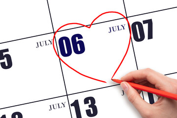 A woman's hand drawing a red heart shape on the calendar date of 6 July. Heart as a symbol of love.