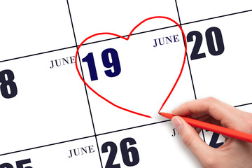 A woman's hand drawing a red heart shape on the calendar date of 19 June. Heart as a symbol of love.