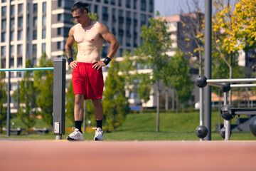 Obraz premium Handsome young muscular man in red shorts at sports ground at public park in summer morning. Sport, fitness, healthy lifestyle concept