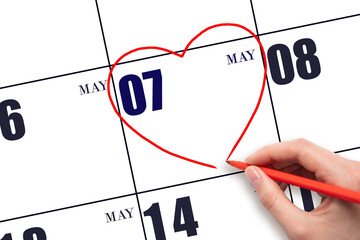 A woman's hand drawing a red heart shape on the calendar date of 7 May. Heart as a symbol of love.