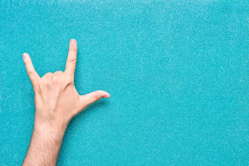 man hand with rock and roll horns gesture coming out from below bright aquamarine background
