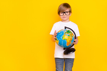 Portrait of handsome cheery intellectual pre-teen boy holding globe copy space explore isolated over bright yellow color background