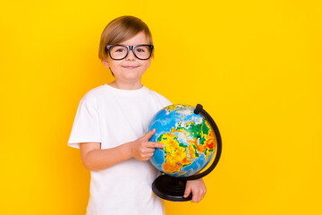 Portrait of handsome cheerful pre-teen boy holding globe finding country explore isolated over bright yellow color background