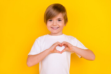 Portrait of handsome kind sweet cheerful pre-teen boy showing heart symbol isolated over bright yellow color background