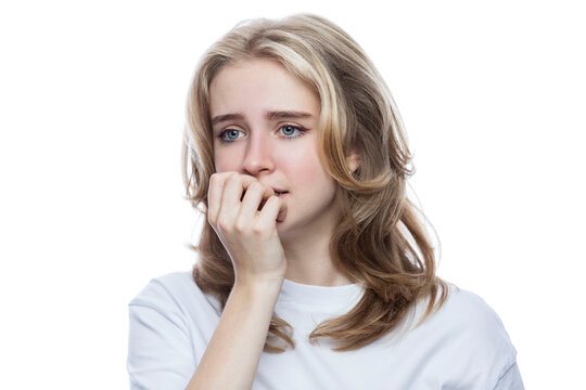 Frightened teenage girl in a white T-shirt bites her nails. Fear and anxiety. Isolated on white background. Close-up.