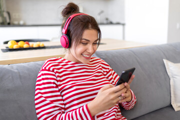 Girl in wireless headphone with phone using mobile player app listening online music. Female learning language, watching movie at home, communicating in social networks, domestic weekend pastime