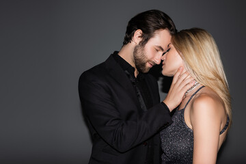 Side view of bearded man in jacket touching blonde girlfriend on grey background.